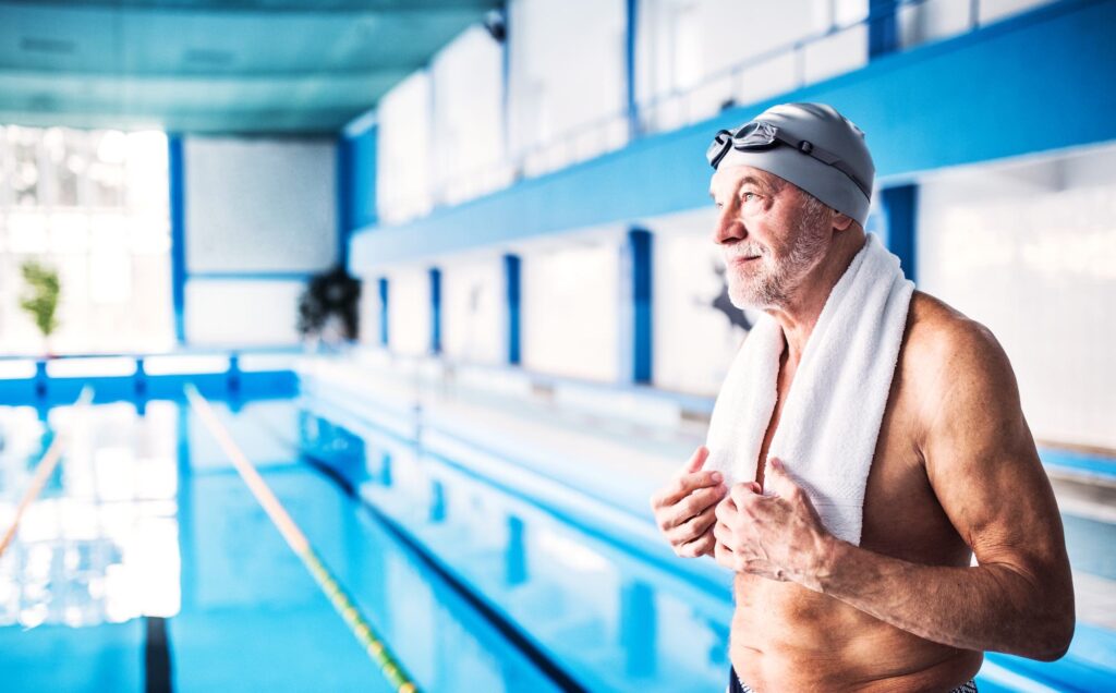 Senior man standing by the indoor swimming pool in Roseville, CA after recovering from shoulder replacement surgery